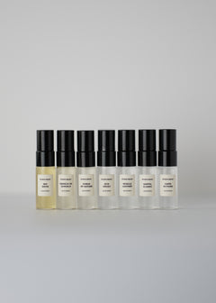Row of seven small fragrance bottles with black caps from the Discovery Set on a light surface