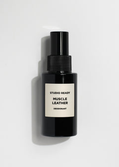 Black spray deodorant bottle labeled Muscle Leather Deodorant on white backdrop.