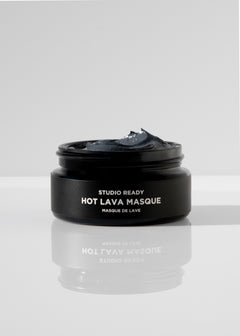 Open black jar of Hot Lava Masque with dark gray paste on a reflective white surface